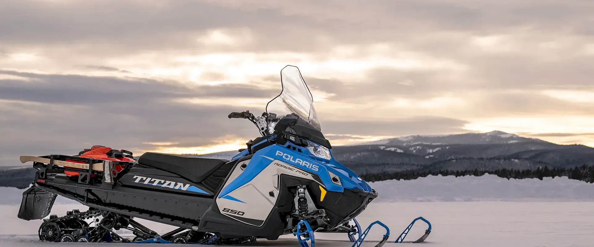 Blue and white Polaris TITAN 850 snowmobile parked on snowy landscape with mountains