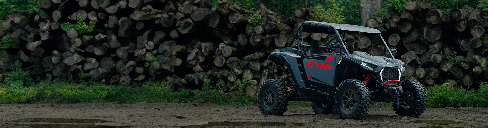 Hero banner showing Polaris RZR parked on mud near stacked logs